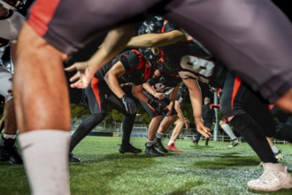 American football players crouched on green artificial turf under stadium lights, lined up for a