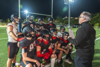 American football coach reviewing game strategy and tactical plays with a kneeling team of young