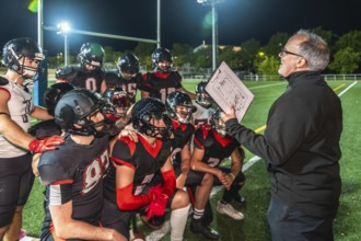 American football coach holds clipboard with play diagram, instructing young athletes in full