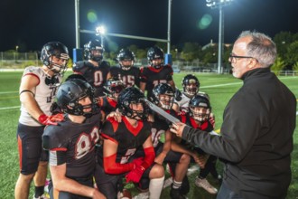 American football coach discussing strategy with his team of players in uniform and helmets during