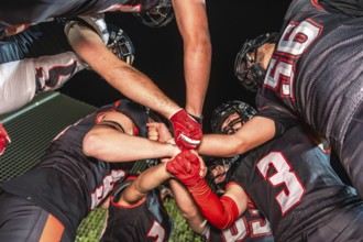 Football teammates in a night huddle, gloved fists stacked in the center, conveying unity,
