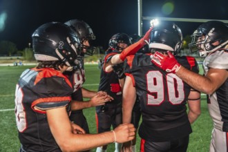 Football teammates huddling on the field under stadium lights at night, celebrating teamwork and