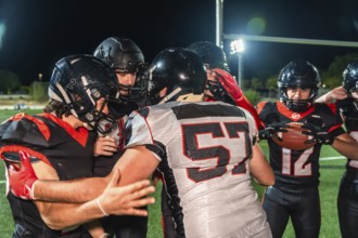 American football players in black and red uniforms with helmets and shoulder pads huddling on a