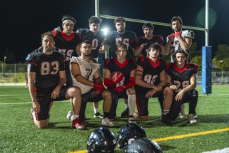 American football team in uniforms posing on illuminated turf at night, holding a ball and