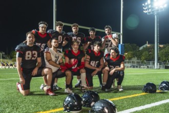 American football players in black and red uniforms posing for a group portrait on a stadium field