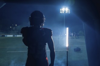 Football player standing in silhouette, ready to enter the stadium field at night, stadium lights