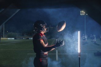 American football player in helmet and uniform lunging to catch a pass under stadium lights, smoke