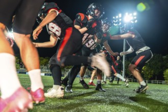 American football players in black and red uniform helmets battling on a green artificial turf