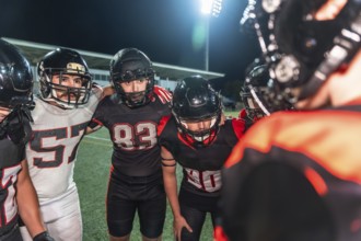American football players in uniform and helmets huddling together with arms around shoulders,