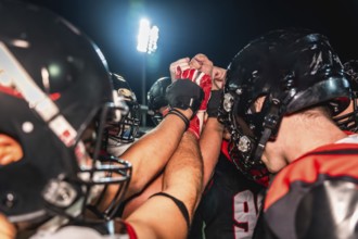 American football players putting hands together in a huddle, symbolizing teamwork, unity,