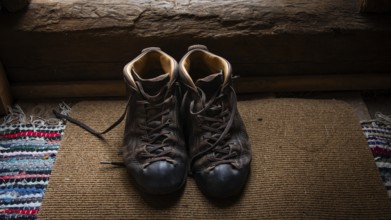 Eingetragene Wanderschuhe auf einem Teppich in einem rustikalen Innenraum, historischer Bauernhof