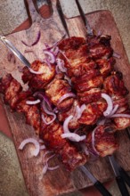 Pork kebab on skewers, with red onion, on a wooden chopping board, close-up, top view