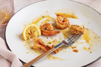 The remains of fried shrimp in oil with spices, on a white plate, with a fork, there are no people