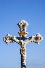 Crucifix with hoarfrost in front of blue sky at sunshine in winter, Bavaria, Germany