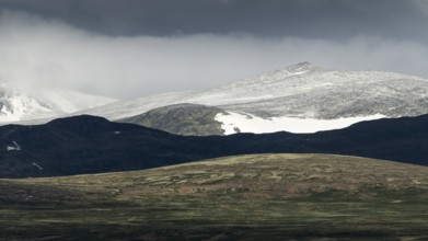 Blick auf schneebedeckten Berggipfel und baumlose Landschaft, dramatische Wolken, Pilgerweg