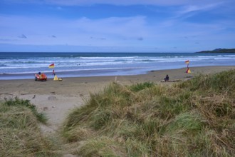 Rettungsflaggen am Strand mit grasbewachsenen Dünen und leichten Wellen im Meer, Kaka Point, Clutha
