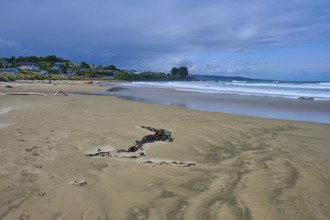 Weitläufiger Strand mit Meer, Wellen und entfernten Häusern unter einem leicht bewölkten Himmel,