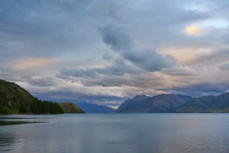 Friedlicher See mit Bergpanorama und bewölktem Himmel kurz vor Sonnenuntergang, Lake Hawea, Hawea,