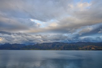Stilles Gewässer vor bergiger Landschaft und dramatischem Himmel in der Dämmerung, Lake Hawea,