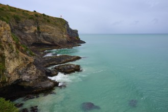 Dramatische Küstenlandschaft mit steilen Klippen Leuchturm und grünlich-blauem Meer unter einem