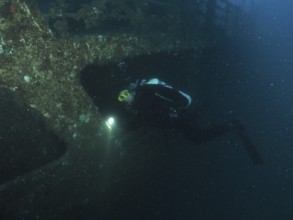 Diver examines a shipwreck with a lamp in the dark. Dive site wreck of the Vis, Pula, Croatia,