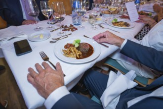 Steak with vegetables and pasta in an elegant table setting with white wine glasses and cloth