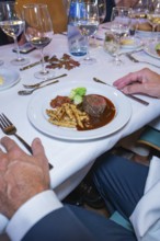 Steak with vegetables and pasta in an upscale dining environment with white tablecloth and wine
