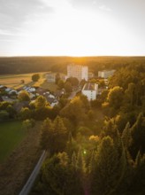 Aerial view of a village at sunset, surrounded by forests and fields, Tesla Model Y Juniper,