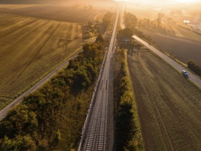 View of railway tracks and neighbouring fields at sunrise in golden light, Hermann Hesse Railway,