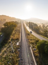 View of railway tracks and country road in the early morning light. Trees and fields frame the