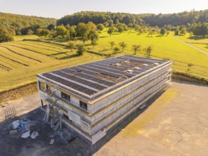 Modern building with solar panels surrounded by fields and forests, under construction, new build