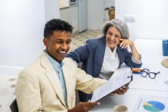 Diverse business professionals sharing a moment of laughter while reviewing documents, fostering