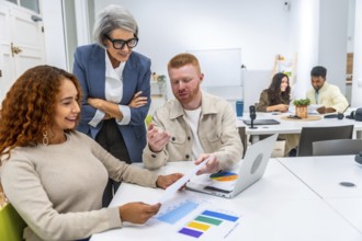 Multigenerational business team discussing charts and data with laptop in a modern coworking