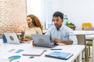 Multiracial customer service team wearing headsets and typing on laptops in a modern office,