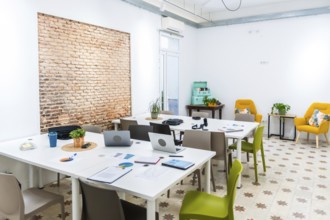 Bright open plan coworking office space featuring long white tables with laptops and charts, a