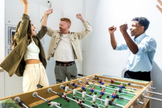 Diverse group of friends raising their arms in celebration after winning a foosball match, enjoying