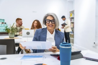 Happy mature businesswoman smiling at the camera, holding charts and graphs during a meeting with