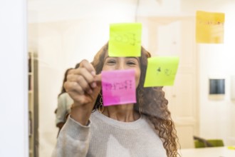 Happy woman collaborating on a project, writing ideas and tasks on colorful sticky notes on a clear