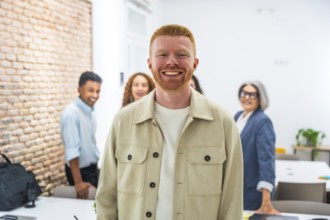 Redhead man standing in front, confidently smiling at the camera, with a diverse business team
