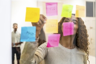 Woman organizing colorful sticky notes on a clear glass board, actively brainstorming and planning