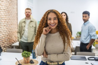 Confident young businesswoman with curly hair smiling at camera. Standing in a contemporary office
