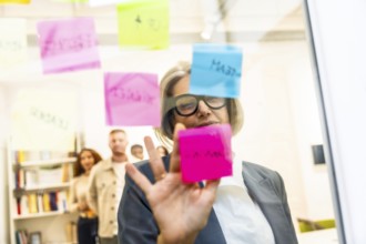 Mature businesswoman arranging colorful sticky notes on a glass board while leading a strategic