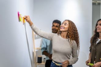 Young diverse team collaborating on a project, happy woman placing a colorful sticky note on a