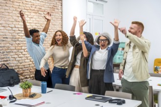 Multiracial business team in a modern office cheering with arms raised, celebrating a shared