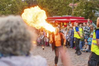 A fire-eater performs an exciting show in front of a large audience on a cobbled street,