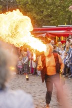 A man breathes fire during a show, surrounded by an attentive audience at a festival, Feuernacht,