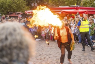A fire-breather entertains the crowd during an outdoor performance, flames shoot out of his mouth,