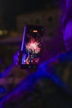 Person holding a mobile phone showing a photo of colourful fireworks at night, Fire Night,