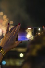 A hand with a mobile phone holds the fireworks in the night, sparkling bokeh, Fire Night,