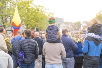 People gather under trees in sunny weather with colourful decorations in the background, Fire